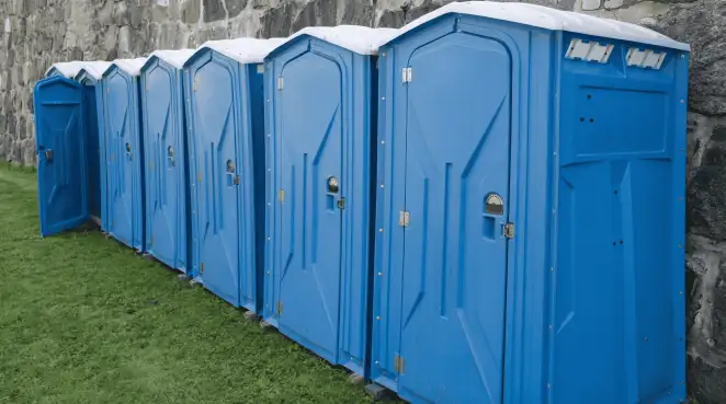 Row of blue portable toilets lined up on grass against a stone wall for event sanitation in Chicago, IL