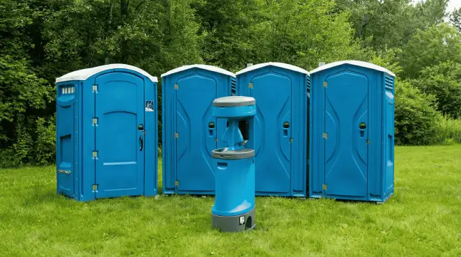 Four blue portable toilets and a matching hand washing station on grass near trees, a common sight at local outdoor events in Chicago, IL