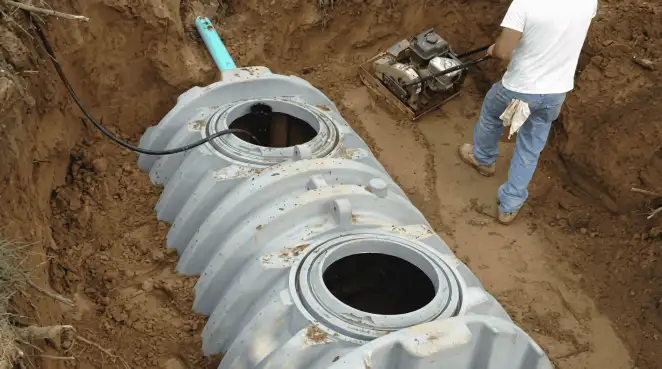 Septic tank installation showing a technician compacting soil around a new poly septic tank in an excavation pit in Chicago, IL
